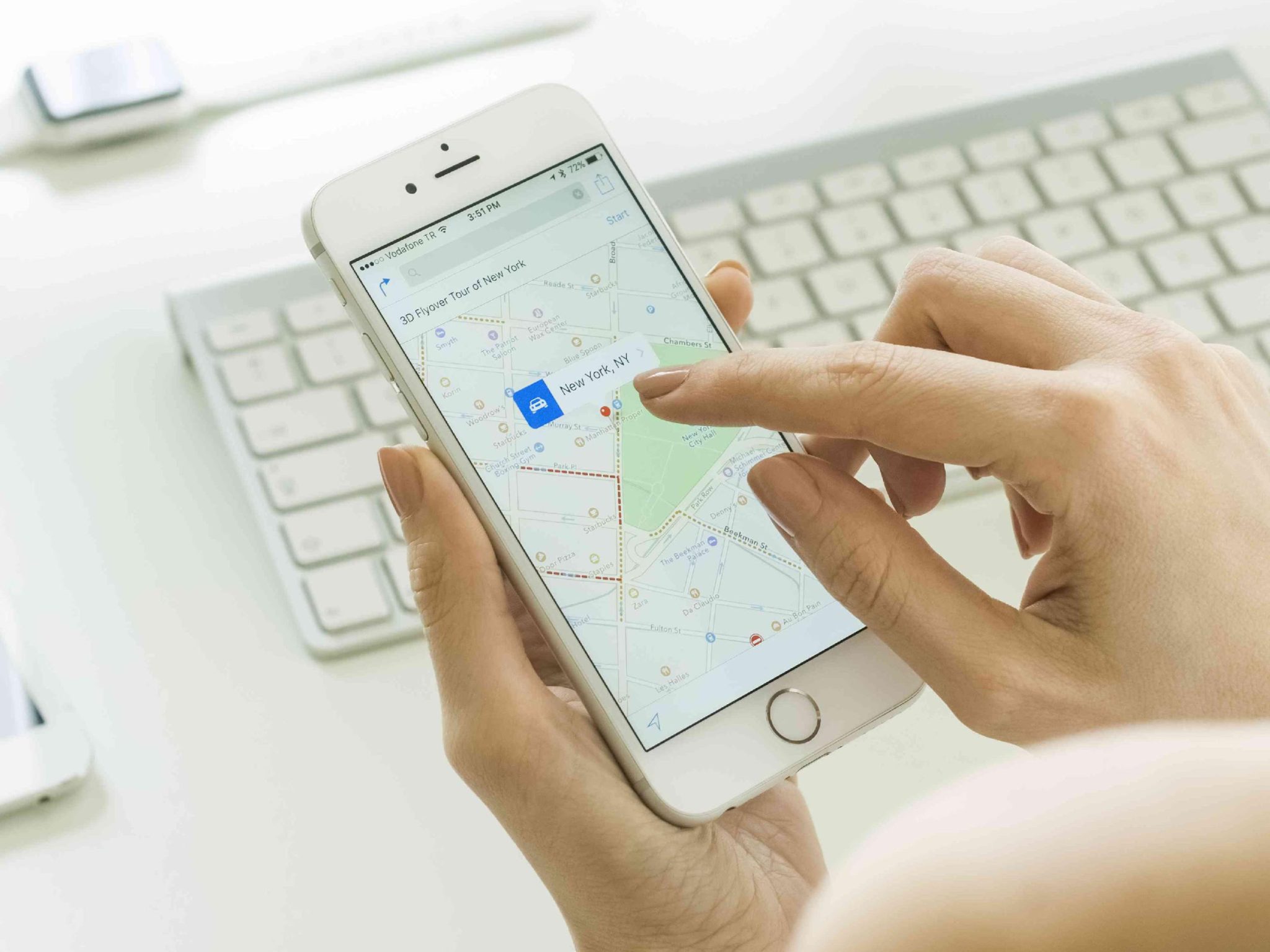  A hand holding a smartphone with a map of New York City and a finger touching the screen with the search query 'GPS tracker for tracking turnedoff cell phone' in the search bar.